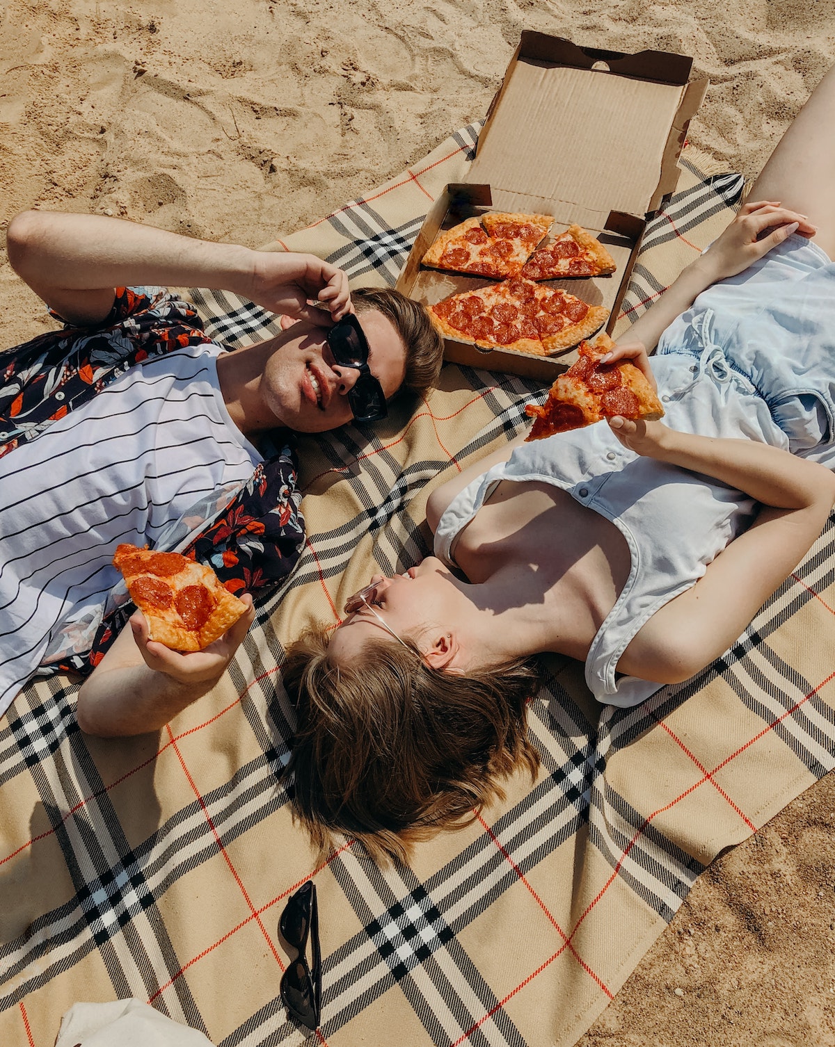 couple eating pepperoni pizza on the beach